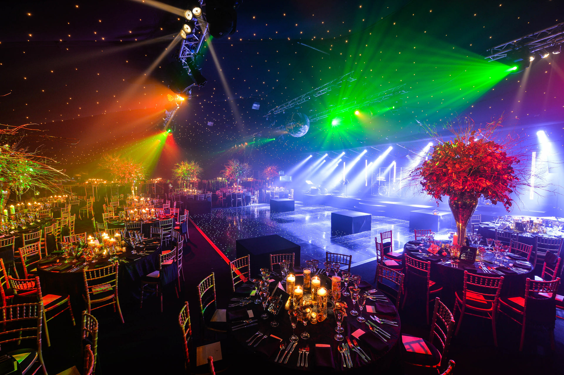 An elegantly decorated corporate event room with dressed tables, candlelight, and a dance floor