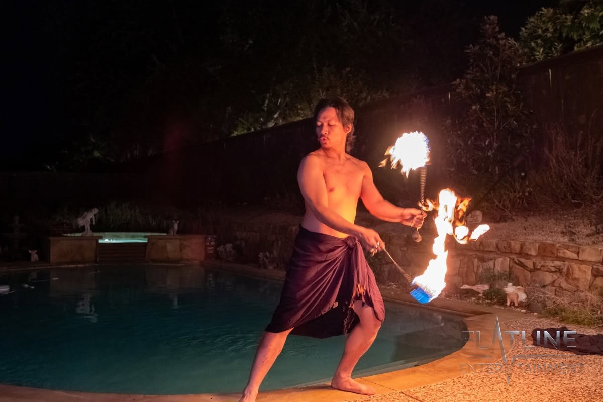 A fire performer spinning flames beside a pool at a birthday party
