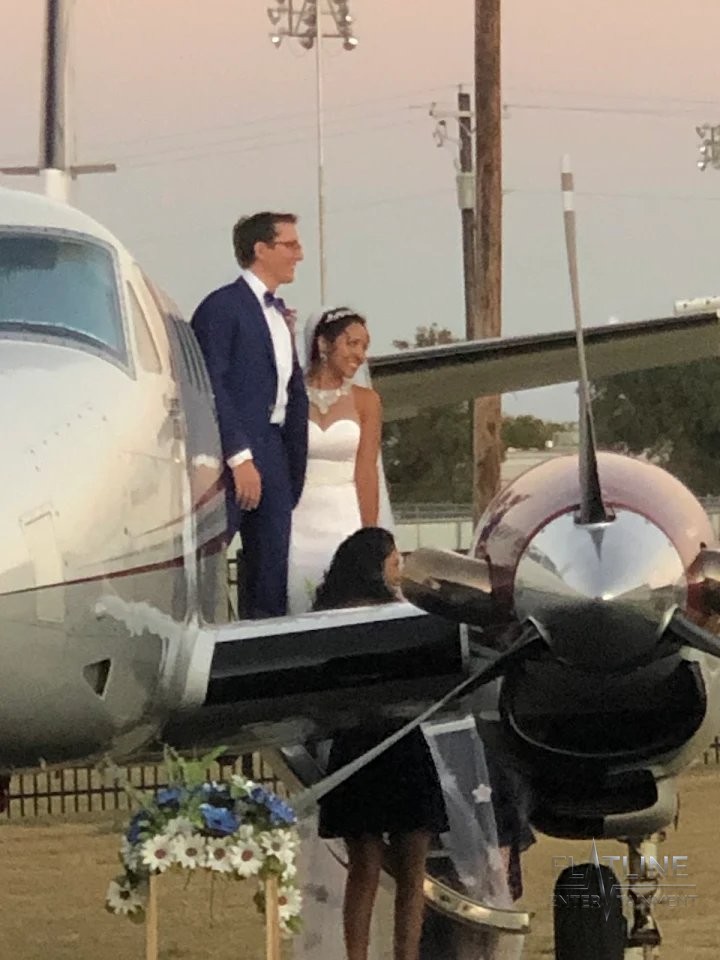 A bride and groom smiling beside a private jet at their wedding